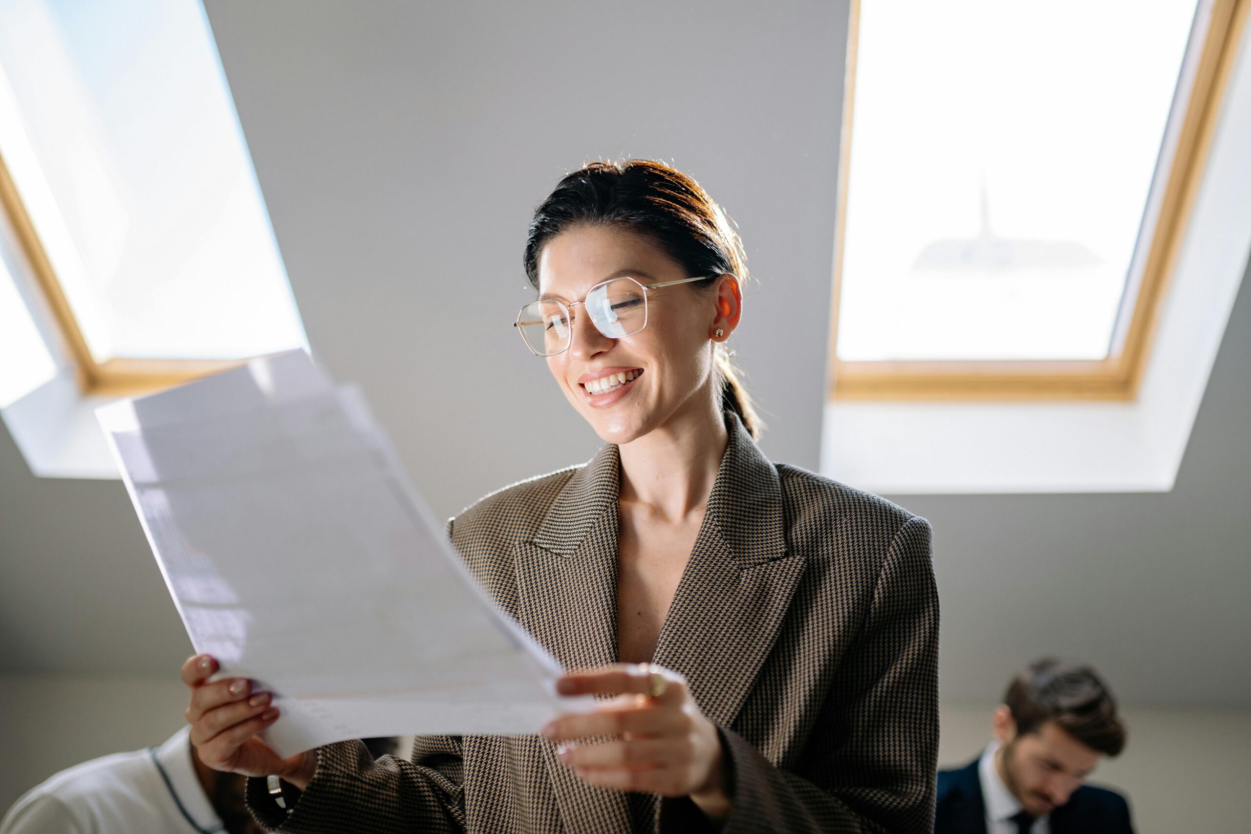 Smiling woman wearing eyeglasses reviewing paperwork in a modern office setting.