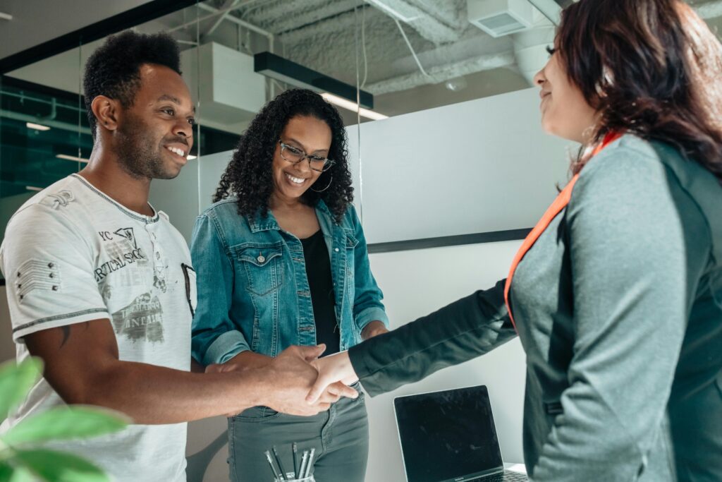 Smiling couple shaking hands with advisor in a modern office, symbolizing collaboration and understanding.