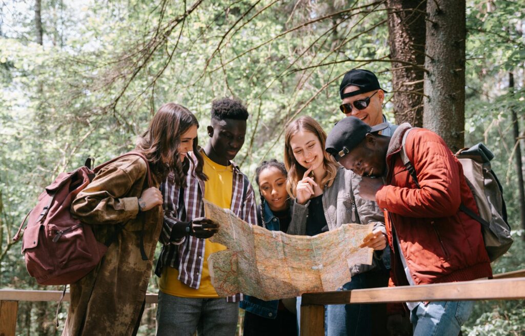 A group of diverse friends walk through a forest trail with a map, highlighting the value of guidance, shared journeys, and learning from experience.