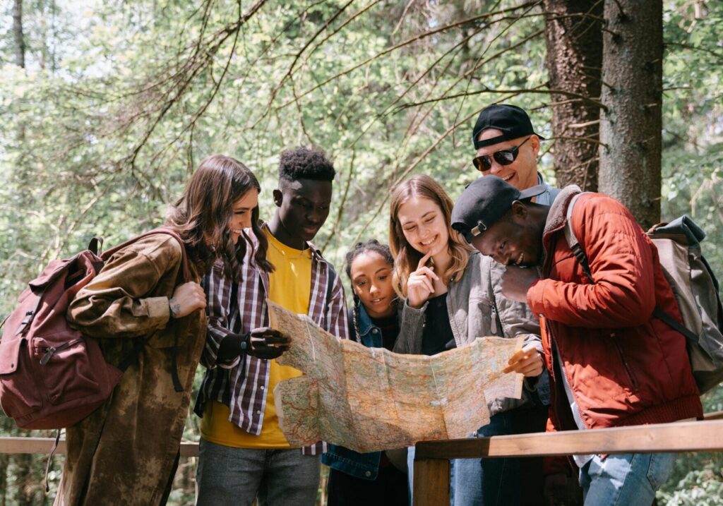 A group of diverse friends walk through a forest trail with a map, highlighting the value of guidance, shared journeys, and learning from experience.