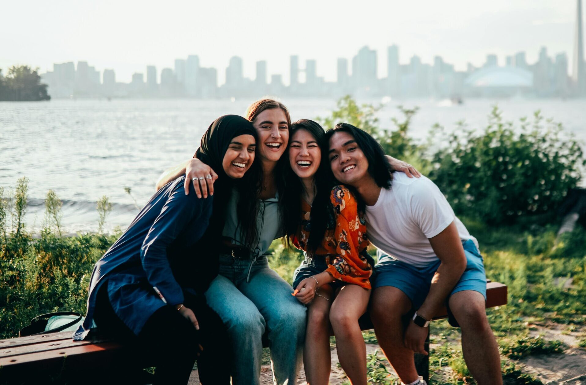 Four friends share a joyful moment with Toronto’s skyline in the background, symbolizing engagement, connection, and visibility in community life.