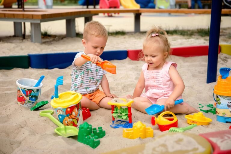 Two kids enjoying playtime with colorful toys in a sunny sandbox.