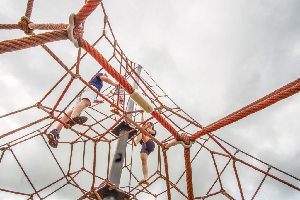 Children climbing on a rope structure under a cloudy sky in an outdoor playground.